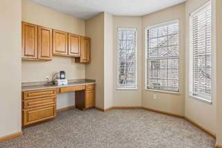 Bright apartment office nook with built-in wood cabinetry, a desk area, carpeted flooring, and three large windows with blinds.