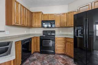U-shaped apartment kitchen with extensive wood cabinetry, wraparound counters, black appliances, and a double-basin sink.