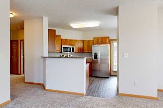 A kitchen with a breakfast bar countertop, wooden cabinets, and stainless steel appliances next to a living room.