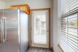 A kitchen with a stainless steel refrigerator with wooden cabinets above it, and a windowed door to the balcony.