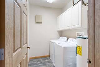 A laundry room with hard wood flooring, full-sized washer and dryer, and four overhead storage cabinets.