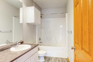 A bathroom with a vanity sink, overhead storage cabinets, and tub shower.