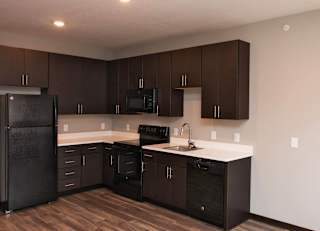 A kitchen with dark brown cabinets and a black refrigerator.