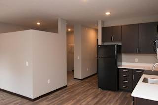 L-shaped kitchen with dark brown cabinets is across from a partial walled sleeping area in a studio apartment