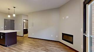 a living room with hardwood floors, an electric fireplace, next to an open kitchen