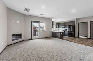 Bright apartment living room with plush carpeting, a modern kitchen, recessed lighting, a fireplace, and a sliding glass door to a private patio.
