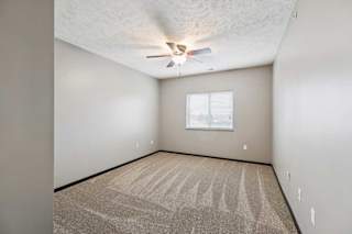 A carpeted bedroom with a large window and a ceiling fan.