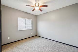 A carpeted bedroom with a window and a ceiling fan.