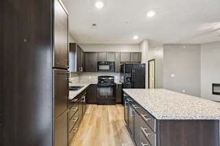 A kitchen with dark cabinets, granite counters, and black appliances.
