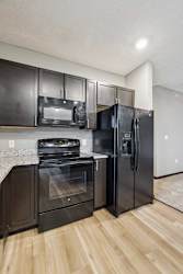 A close up of a black range and microwave in a modern kitchen with dark cabinets and light granite countertops.
