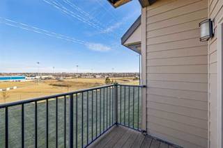 Private apartment balcony with wood-style flooring and metal railing overlooking open green space and nearby buildings.
