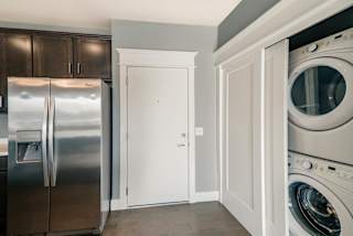 A kitchen with a refrigerator, a door to hallway and closet with stacked washer and dryer.