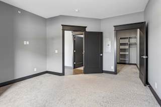 Carpeted apartment bedroom with gray walls, bold dark trim, and direct access to a walk-in closet with built-in shelving.