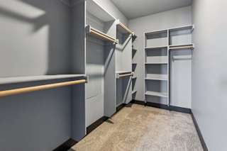 Built-in closet system offers open shelving and hanging rods on multiple walls, with gray finishes and neutral carpeting.