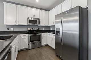 Stainless steel refrigerator, oven, and microwave stand out against crisp white cabinets and dark counters in this apartment kitchen.