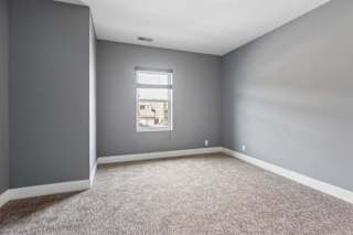 Soft natural light enters this unfurnished apartment bedroom, highlighting gray walls, neutral carpeting, and crisp white trim.