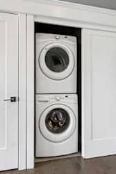 Stacked washer and dryer fit neatly into a recessed apartment laundry closet with white sliding doors and trim.