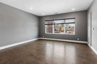 Expansive apartment living room features wood-look flooring, gray walls, and a broad window overlooking the surrounding community.
