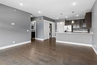 Open apartment living area leads into a kitchen with dark cabinetry, a breakfast bar, pendant lighting, and nearby in-home laundry.