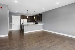 Generous living area with wood-look flooring opens to a dark-cabinet kitchen, breakfast bar, and stainless steel appliances.