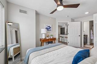 Apartment bedroom with ceiling fan, full-length mirror, and neutral finishes.