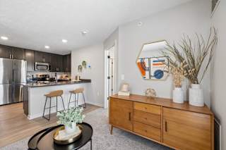 Open-concept apartment living area with a kitchen island, bar seating, stainless steel appliances, and modern furnishings.