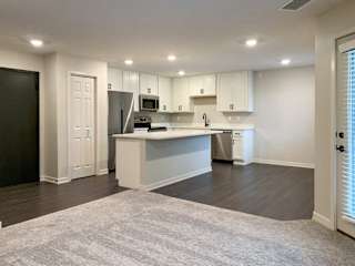 modern kitchen with white cabinets and a island with wood look flooring and carpet