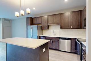 A kitchen with dark wood cabinets, quartz countertops, a large island, stainless steel appliances, and a designer backsplash.