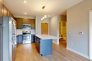 A kitchen with dark wood cabinets, quartz countertops, a large island, stainless steel appliances, and a designer backsplash.