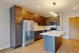 A kitchen with dark wood cabinets, quartz countertops, a large island, stainless steel appliances, and a designer backsplash.