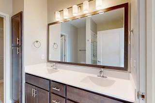 A bathroom with a double sink marble vanity, oversized mirror, and dark wooden cabinets.