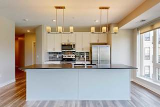 A kitchen with white wooden cabinets, quartz countertops, a large island, stainless steel appliances, and a designer backsplash.