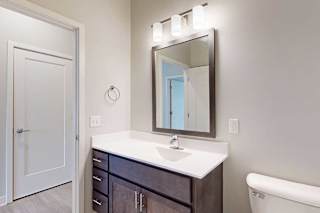 A bathroom with a marble vanity, dark wooden cabinets, and a mirror with overhead lighting.