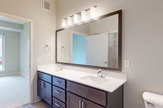 A bathroom with a double sink marble vanity, oversized mirror, dark wooden cabinets, and a door open to a bedroom.