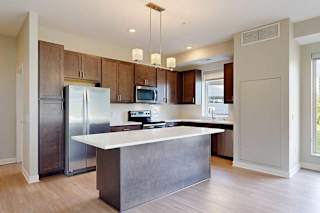 A kitchen with dark wood cabinets, quartz countertops, a large island, stainless steel appliances, and a designer backsplash.