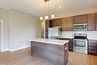 A kitchen with dark wood cabinets, quartz countertops, a large island, stainless steel appliances, and a designer backsplash.