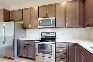 A kitchen with dark wood cabinets, quartz countertops, stainless steel appliances, and a designer backsplash.
