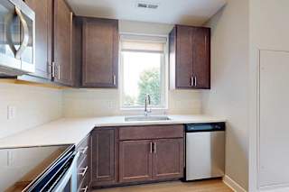 A kitchen with dark wooden cabinets, quartz countertops, a tile backsplash, an island, and a window over the kitchen sink.