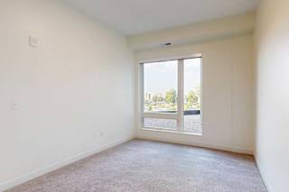 apartment bedroom with a large window and a carpeted floor.