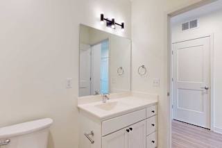 Minimalist bathroom with white walls and cabinetry, a rectangular mirror, and a modern black light fixture.