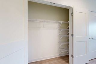 Open closet with white double doors, featuring empty white wire shelves on the right and a light beige interior