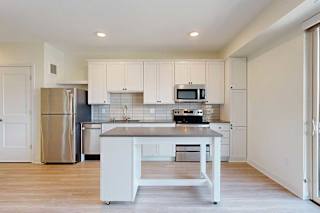 A kitchen with white cabinets and a stainless steel refrigerator, plus a central island