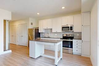 Modern kitchen with white cabinets, stainless steel appliances, and wooden floors. Central island, backsplash tiles, and bright lighting create a clean, inviting ambiance.