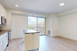 A modern, bright kitchen with white cabinets, stainless steel appliances, and a small island. A large window with a view of a building outside adds natural light.
