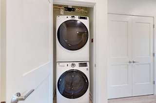 Stacked washer and dryer in a small, open closet with white doors, creating a compact and modern laundry space.