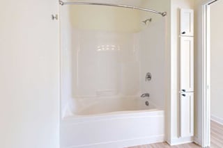 A clean, white bathroom featuring a bathtub with a shower, a curved curtain rod, and adjacent storage cabinets.