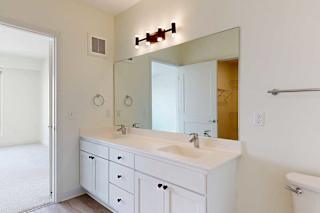 Modern bathroom with a large mirror, double sinks, white cabinetry, and overhead lighting. Neutral tones create a clean and spacious feel.