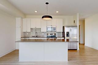 Modern kitchen featuring white cabinets, stainless steel appliances, and a spacious island with a sleek countertop and pendant lighting.