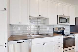 Modern kitchen with white cabinets, gray tile backsplash, stainless steel sink, dishwasher, and appliances.