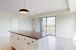 A bright, modern kitchen with white cabinets, a dark wood island, and a sleek hanging light. Glass doors open to a balcony with a scenic view.